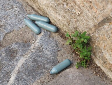 Quatre cartouches de protoxyde d'azote jetées au sol, sur un trottoir.